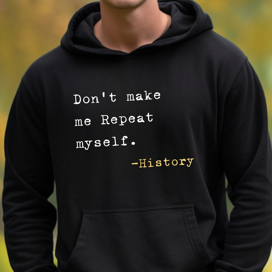 A person wearing a black hoodie with a printed quote on the chest that reads 'Don't make me Repeat myself. -History' in white and yellow text, photographed outdoors with a blurred green background.