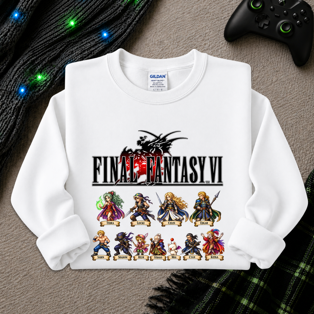 A white Gildan sweatshirt featuring a Final Fantasy VI graphic print, laid flat on a gray textured surface with a black controller, green lights, and a plaid blanket in the background.