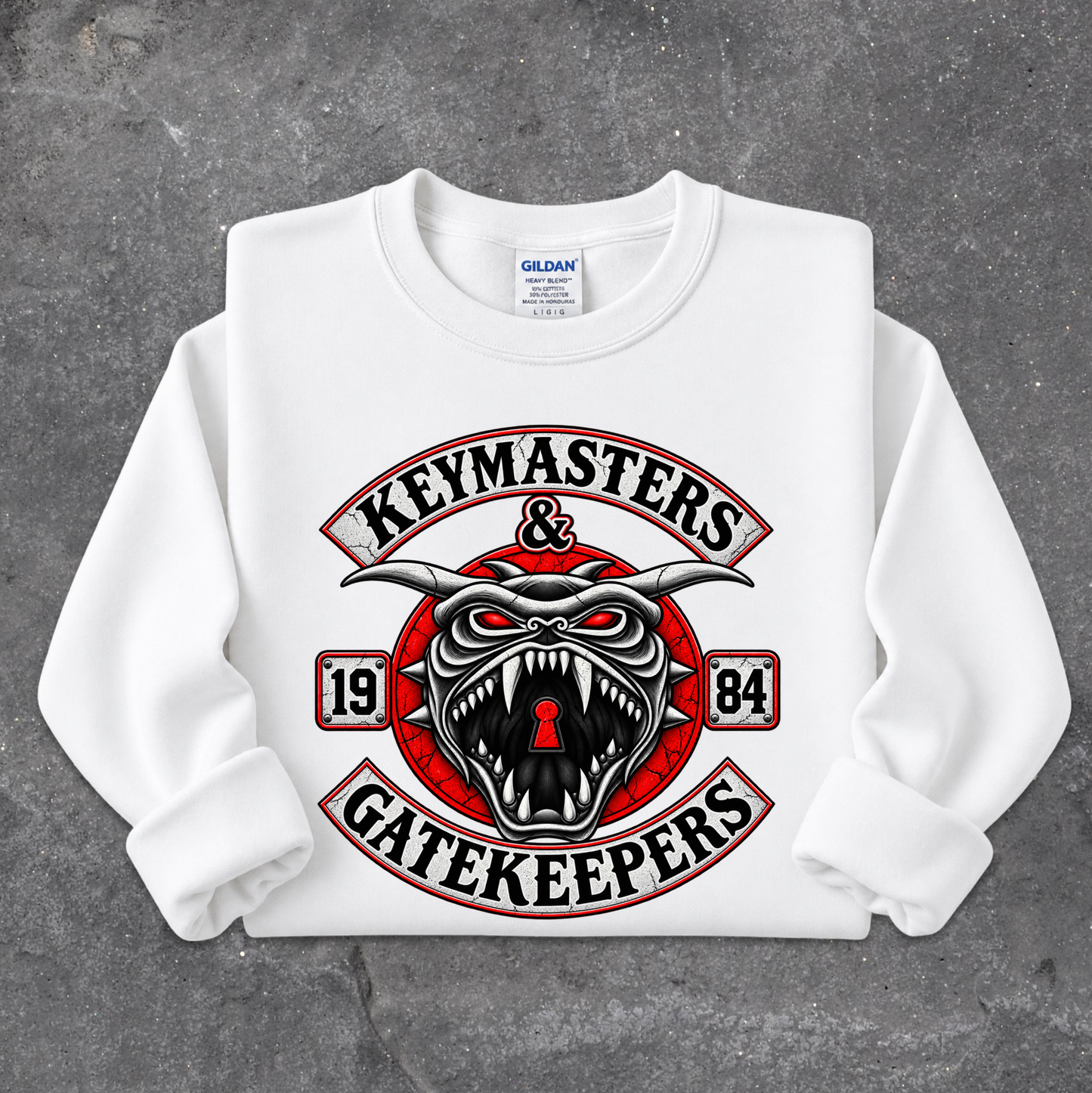 A white long-sleeve crewneck sweatshirt with a large graphic print on the front. The graphic features a red and black snarling horned demon face with a keyhole in its mouth, surrounded by the words 'KEYMASTERS & GATEKEEPERS' in an arch, with '1984' on either side.