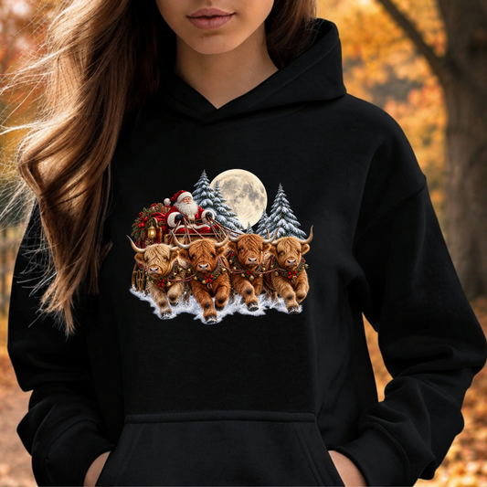 A woman wearing a black hoodie with a colorful graphic print of Santa Claus, a full moon, and four Highland cattle in a snowy landscape, set against an autumn outdoor background.
