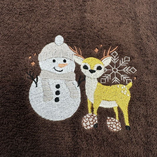 A close-up of a brown textured fabric featuring embroidered winter characters, including a white snowman and a yellow deer with a white snowflake motif.