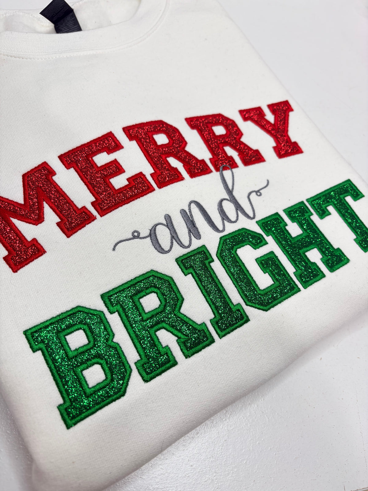 merry and bright in red glitter applique embroidered on a white sweatshirt