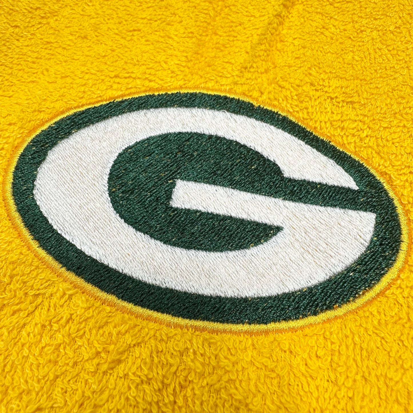 Close-up of a yellow textured fabric with a large embroidered Green Bay Packers logo featuring a white and dark green 'G'.