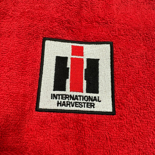 A close-up of a red textured fabric, likely a towel or blanket, featuring a square embroidered patch with the International Harvester logo and brand name.