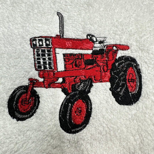 An embroidered red tractor design on a white textured fabric background.