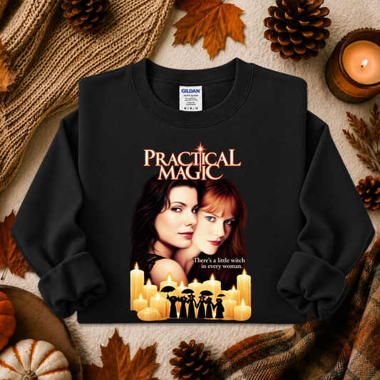 A black long-sleeve crewneck sweatshirt featuring a 'Practical Magic' movie graphic print, styled in a flat-lay with autumn props like pinecones, leaves, and a candle.