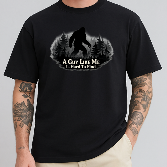 A man wearing a black short-sleeve t-shirt with a graphic of a Bigfoot silhouette in a pine forest and the text 'A GUY LIKE ME IS HARD TO FIND'.