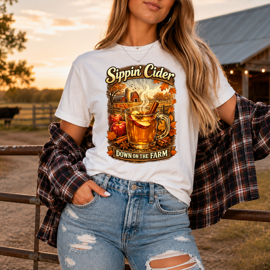 woman wearing a white tshirt with fall autumn farm scene with a glass of apple cider graphic that says sippin cider down on the farm