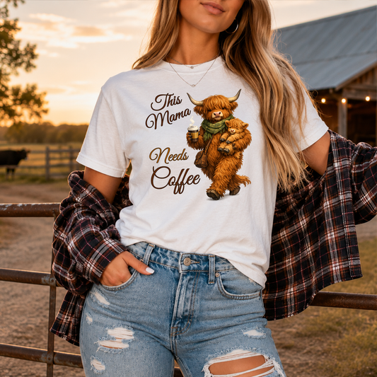woman wearing a white tshirt with a highland cow holding her calf and a cup of coffee that says this mama needs coffee