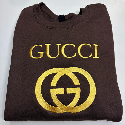 Folded brown sweatshirt with gold Gucci logo on a white background