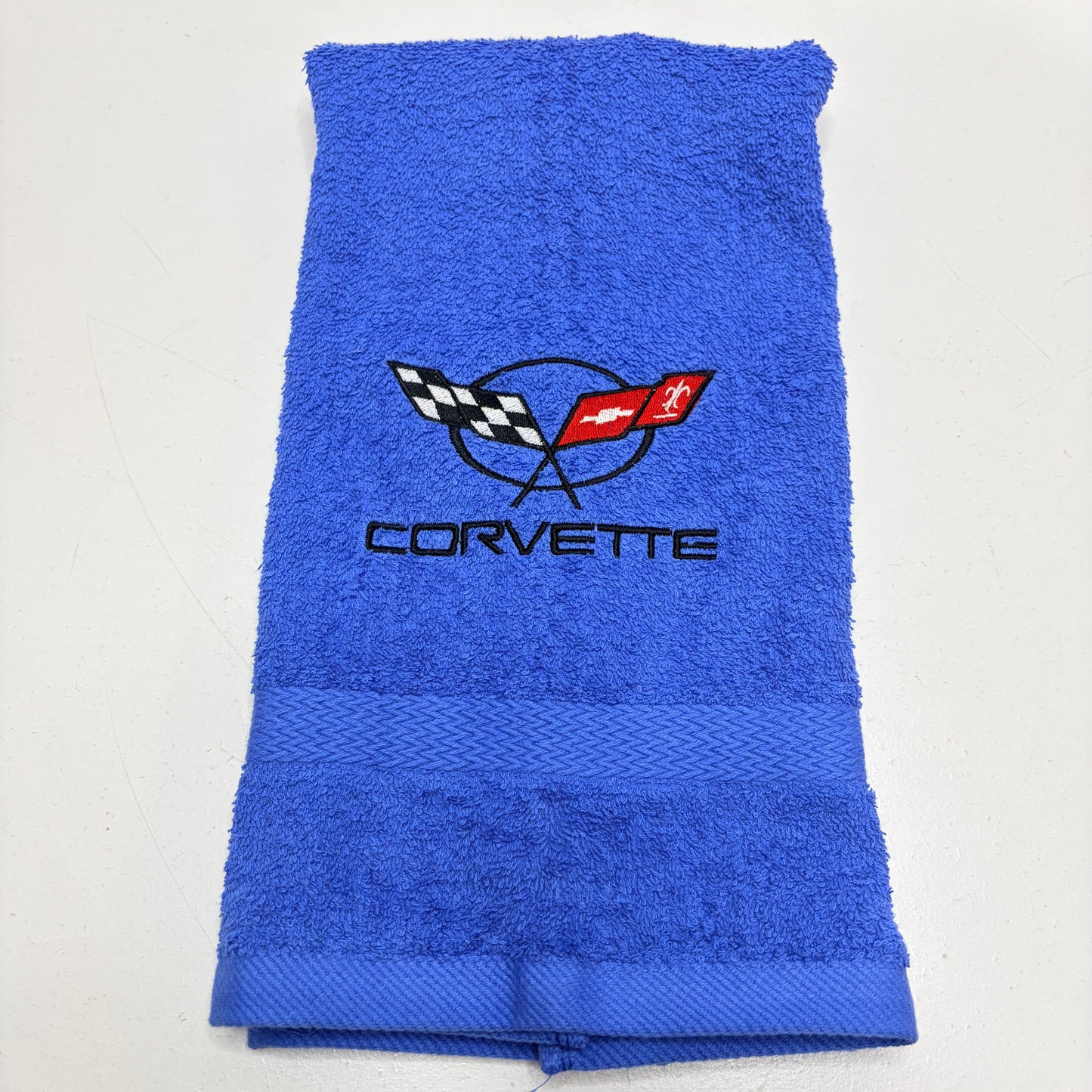 A folded blue terry cloth towel featuring an embroidered Corvette logo in the center, displayed on a plain white background.