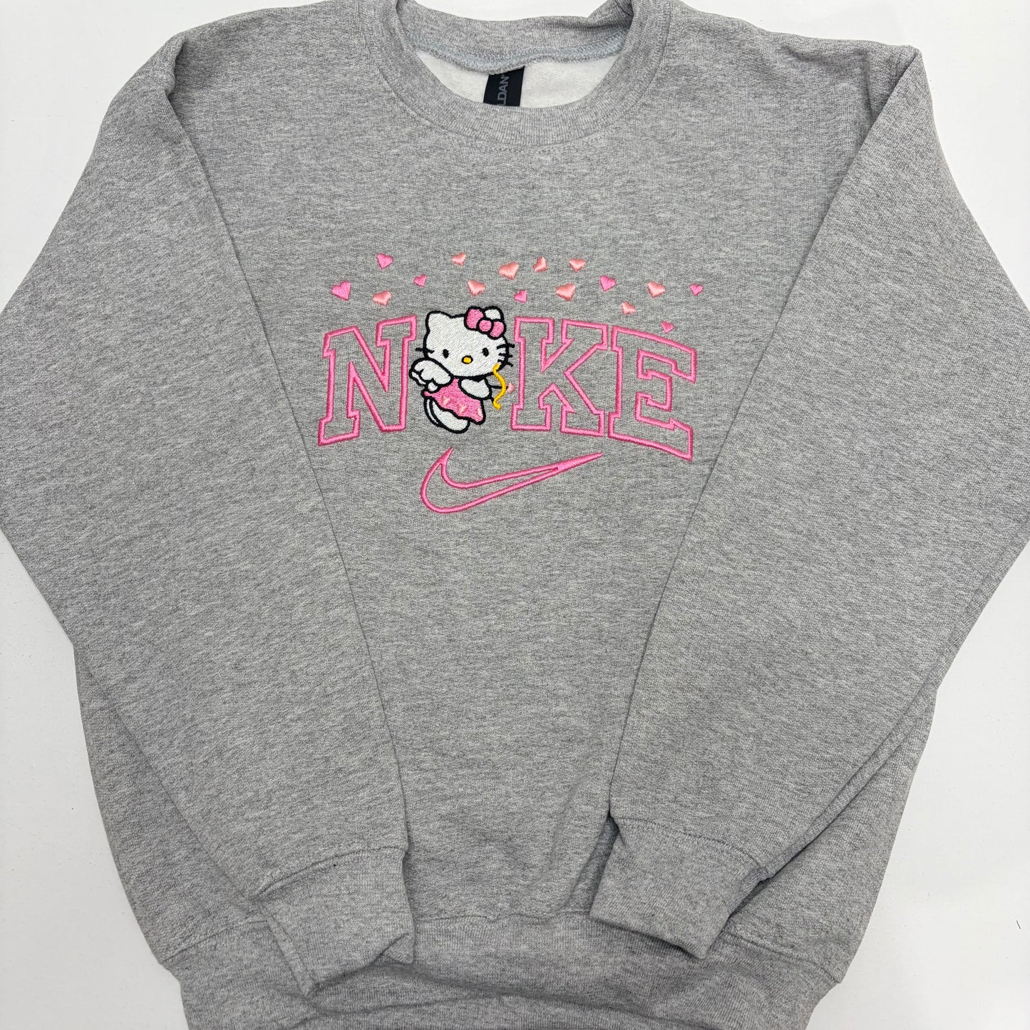 A heather gray crewneck sweatshirt featuring a pink and white Hello Kitty and Nike graphic on the chest, laid flat on a white background.