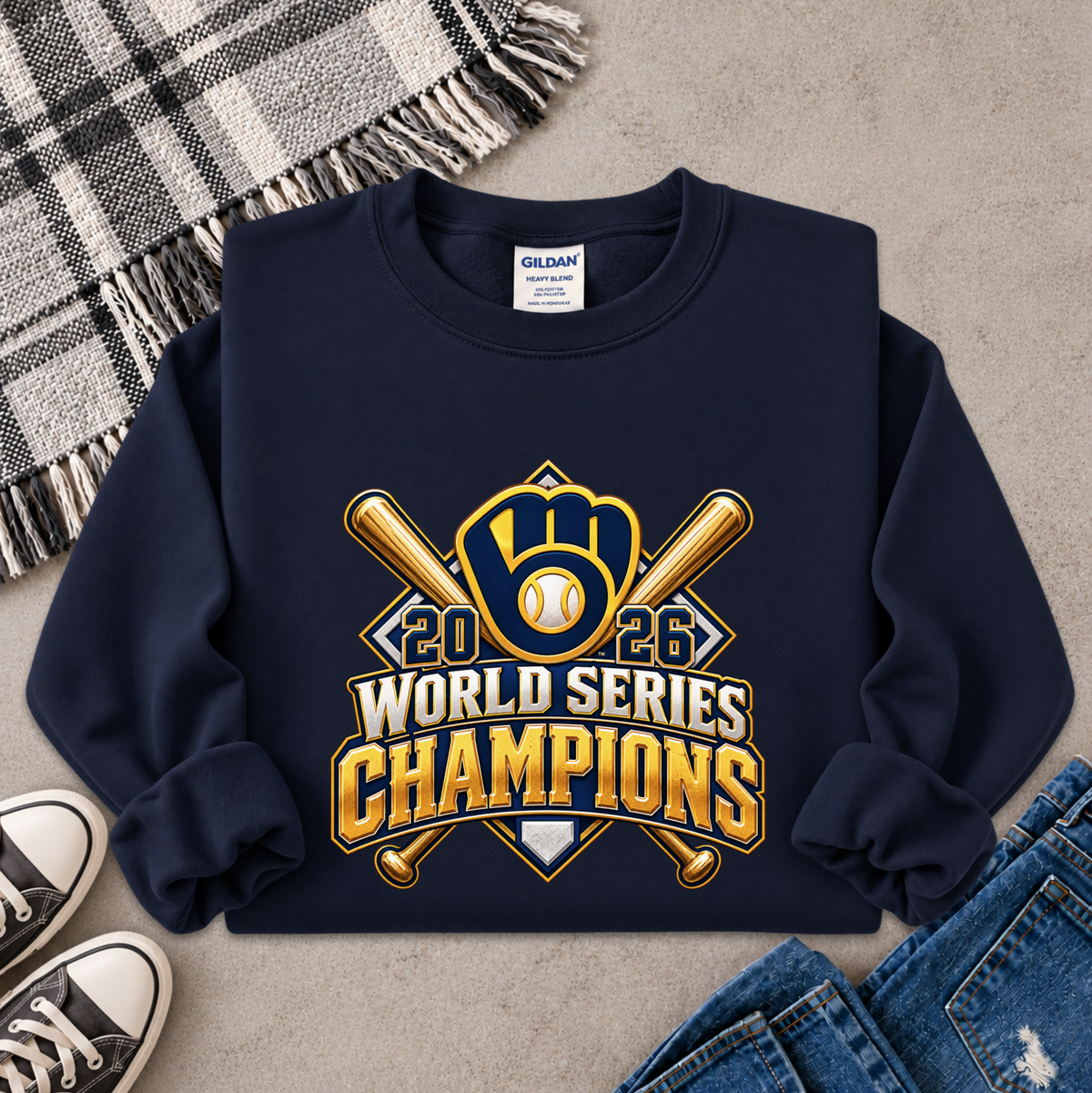 A navy blue crewneck sweatshirt with a '2026 World Series Champions' baseball graphic, styled in a flat lay with a plaid blanket, sneakers, and jeans on a gray concrete background.