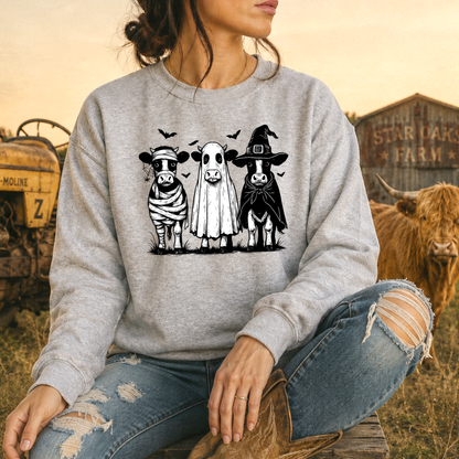 woman wearing gray sweatshirt with funny graphic of 3 cow dressed up in halloween costumes