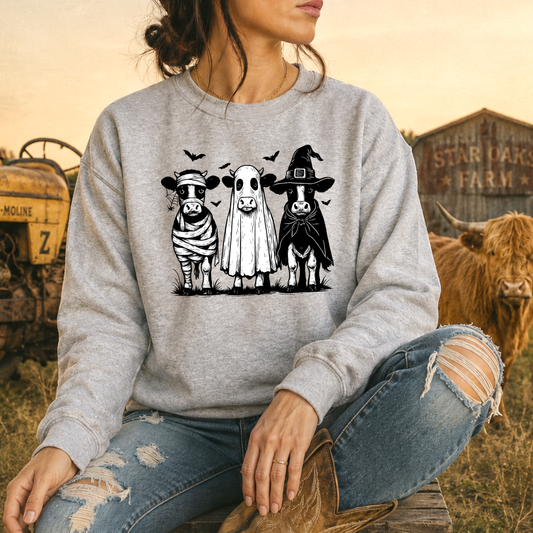woman wearing gray sweatshirt with funny graphic of 3 cow dressed up in halloween costumes