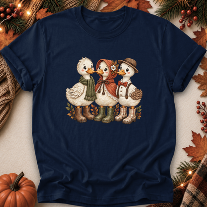 A navy blue short-sleeve t-shirt with a vintage-style graphic of three cute ducks dressed in autumn clothing, laid flat on a neutral background with seasonal props like a pumpkin, pine branches, and fall leaves.