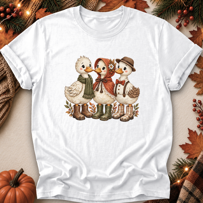 A white short-sleeve crewneck t-shirt featuring a vintage-style graphic of three cute ducks dressed in autumn clothing, surrounded by a cozy fall-themed flat-lay background with a pumpkin, pine branches, and leaves.