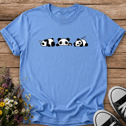 A light blue short-sleeve t-shirt with a cute cartoon panda graphic, laid flat on a rustic wooden background with wildflowers and black-and-white sneakers as props.