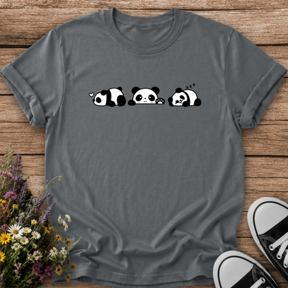 A dark gray crewneck t-shirt featuring a cute graphic of three sleeping pandas in black and white, laid flat on a rustic wooden background with wildflowers and black-and-white sneakers as props.