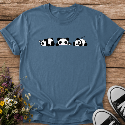 A slate blue short-sleeve t-shirt with a cute cartoon panda graphic, laid flat on a rustic wooden background with wildflowers and black-and-white sneakers as props.