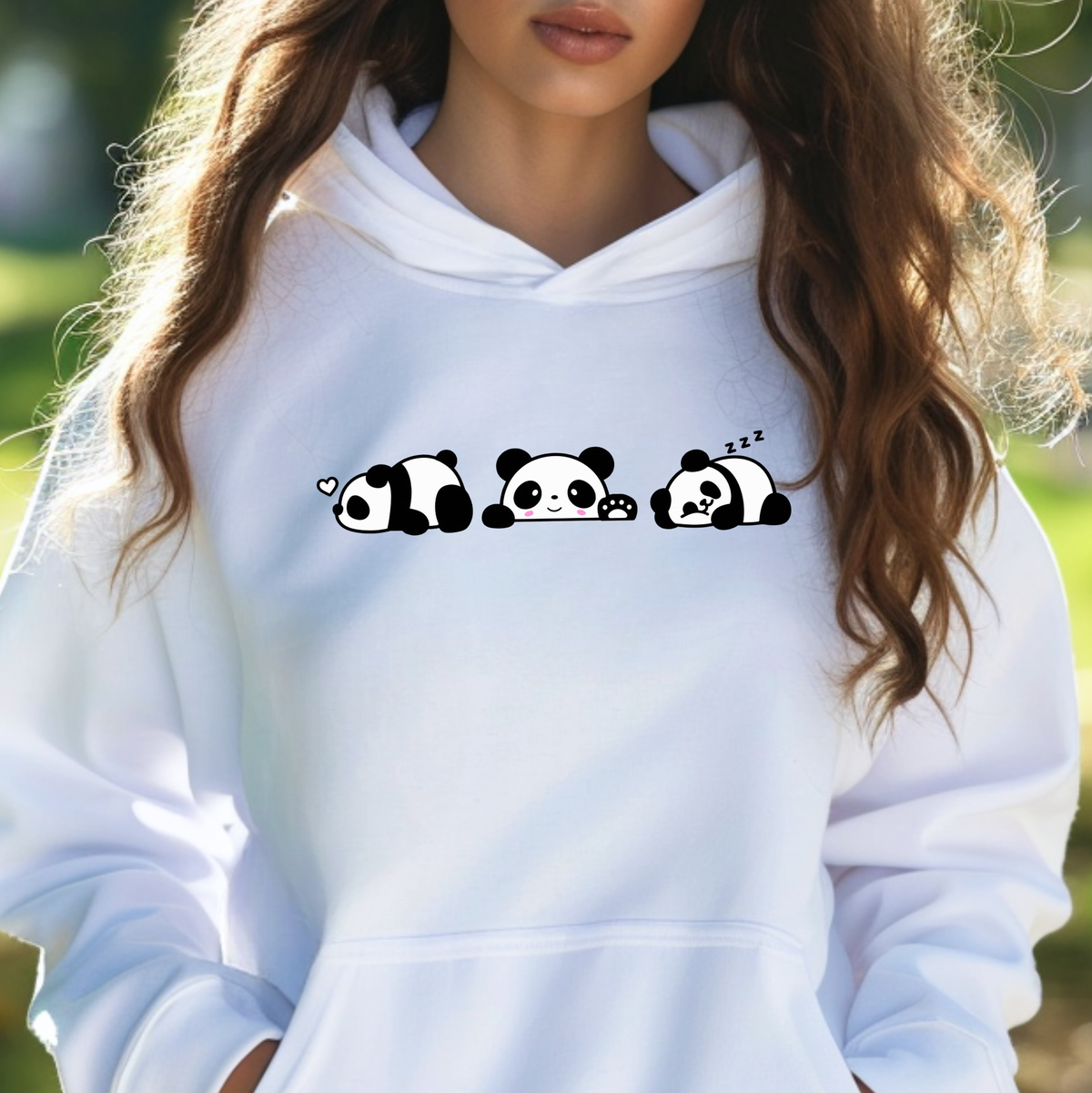 A woman wearing a white pullover hoodie with a black and white cartoon panda graphic across the chest, photographed outdoors with a blurred green background.