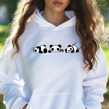A woman wearing a white pullover hoodie with a black and white cartoon panda graphic across the chest, photographed outdoors with a blurred green background.