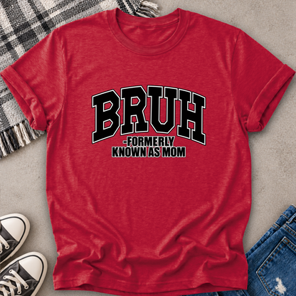 A heather red short-sleeve t-shirt with a black and white graphic reading 'BRUH -FORMERLY KNOWN AS MOM', styled in a flat lay with jeans, sneakers, a plaid blanket, and a gray concrete surface.