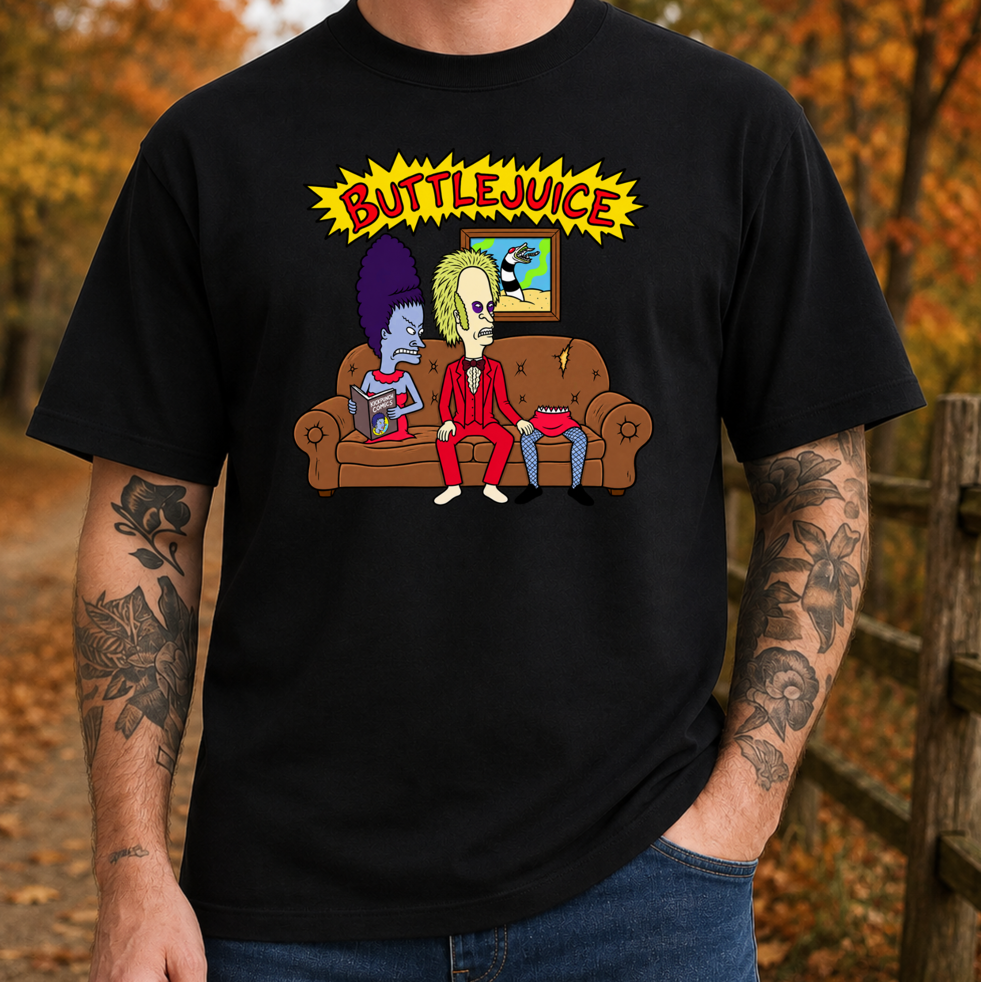 A man wearing a black graphic t-shirt with a cartoon illustration of two characters sitting on a couch under a yellow 'BUTTLJUICE' sign, set against an outdoor autumn background.