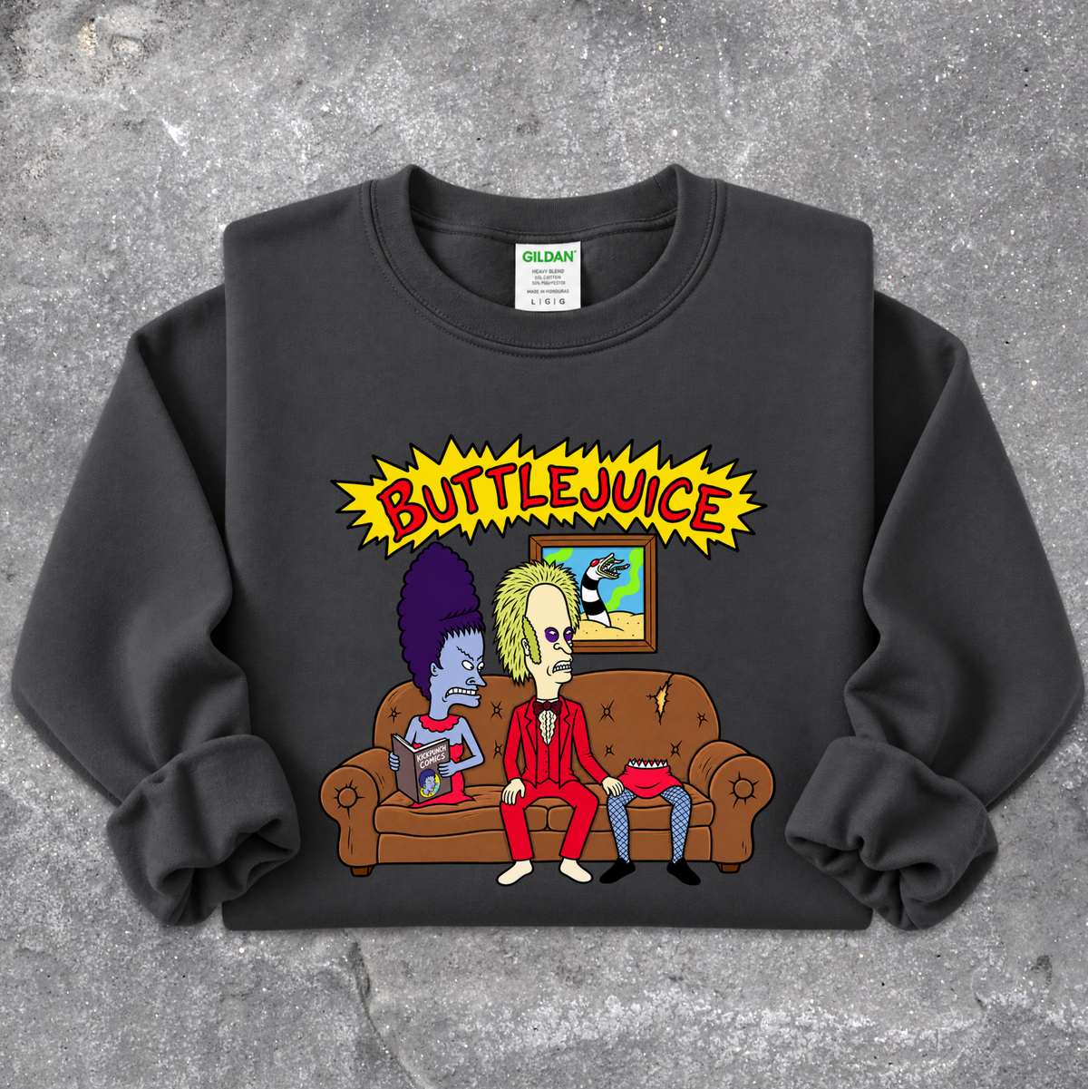 A black Gildan sweatshirt featuring a colorful graphic print of two cartoon characters sitting on a brown couch under a yellow 'BUTTLEJUICE' starburst, laid flat on a gray concrete-textured background.