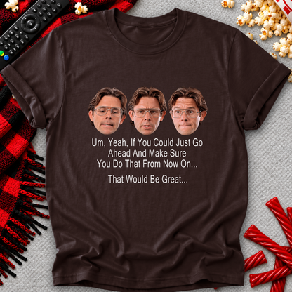 A dark brown graphic t-shirt laid flat on a gray textured background, surrounded by holiday-themed props including a red and black plaid blanket, popcorn, candy canes, and a remote control. The t-shirt features three printed faces of a man with glasses and the text 'Um, Yeah, If You Could Just Go Ahead And Make Sure You Do That From NOW ON.