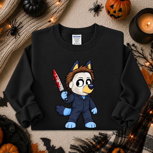 A black crewneck sweatshirt featuring a cartoon graphic of a wolf character in a blue jumpsuit holding a bloody knife, styled in a Halloween-themed flat lay with pumpkins, spider decorations, and a candle.