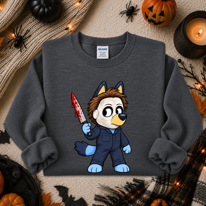 A dark gray crewneck sweatshirt featuring a cartoon graphic of a dog character in a blue jumpsuit holding a bloody knife. The sweatshirt is displayed in a flat-lay Halloween setting with pumpkins, a candle, and spider decorations.