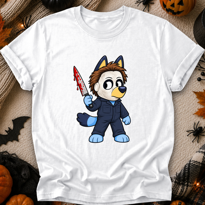 A white short-sleeve crewneck t-shirt featuring a cartoon graphic of a dog character in a blue jumpsuit holding a bloody knife, styled in a flat-lay with Halloween decorations.