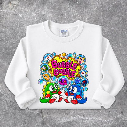 A white long-sleeve crewneck sweatshirt with a colorful cartoon graphic on the front. The graphic features the text 'Bubble Bobble' in pink and yellow, surrounded by various colorful cartoon characters inside bubbles, set against a gray concrete-textured background.