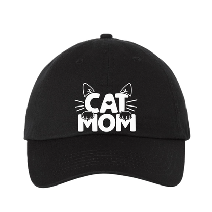 A black baseball cap with a white graphic on the front that reads 'CAT MOM' with cat ears, whiskers, and paws, shown on a plain white background.
