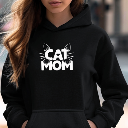 A woman wearing a black pullover hoodie with a white graphic print that reads 'CAT MOM' with cat ears and paw prints, shown in a close-up lifestyle shot.