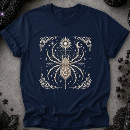 A navy blue short-sleeve t-shirt with a detailed cream-colored gothic graphic of a spider, moon, sun, and stars, laid flat on a textured gray background with dark decorative props.