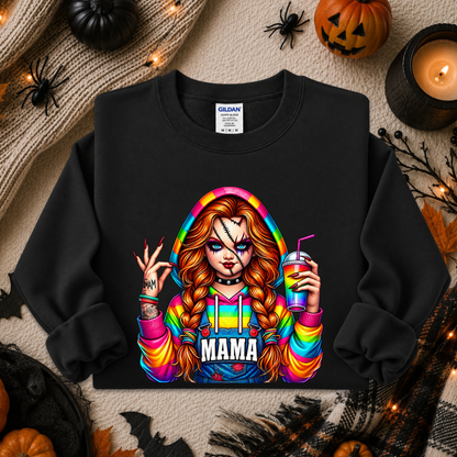 A black crewneck sweatshirt laid flat on a cozy autumn-themed background. The sweatshirt features a colorful graphic of a woman with long red-blonde braids, a bandage over one eye, holding a drink, with the word 'MAMA' printed below.