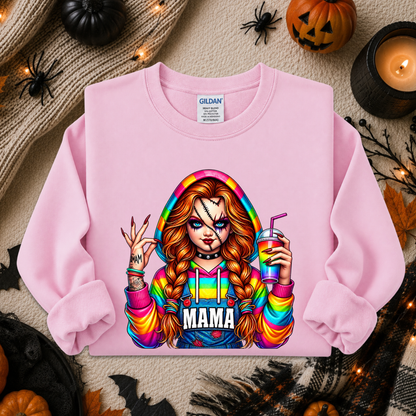 A light pink crewneck sweatshirt by Gildan, featuring a colorful graphic of a woman with long red-blonde braids holding a drink, with the word 'MAMA' printed below. The sweatshirt is displayed in a flat-lay arrangement with Halloween decorations including a pumpkin, spider, candles, and a knit sweater.