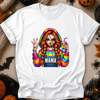 A white short-sleeve crewneck t-shirt featuring a colorful graphic of a horror character with braided hair, rainbow-striped sleeves, and the word 'MAMA' across the chest, displayed on a cozy Halloween-themed background with pumpkins, spider decorations, and a jack-o'-lantern.