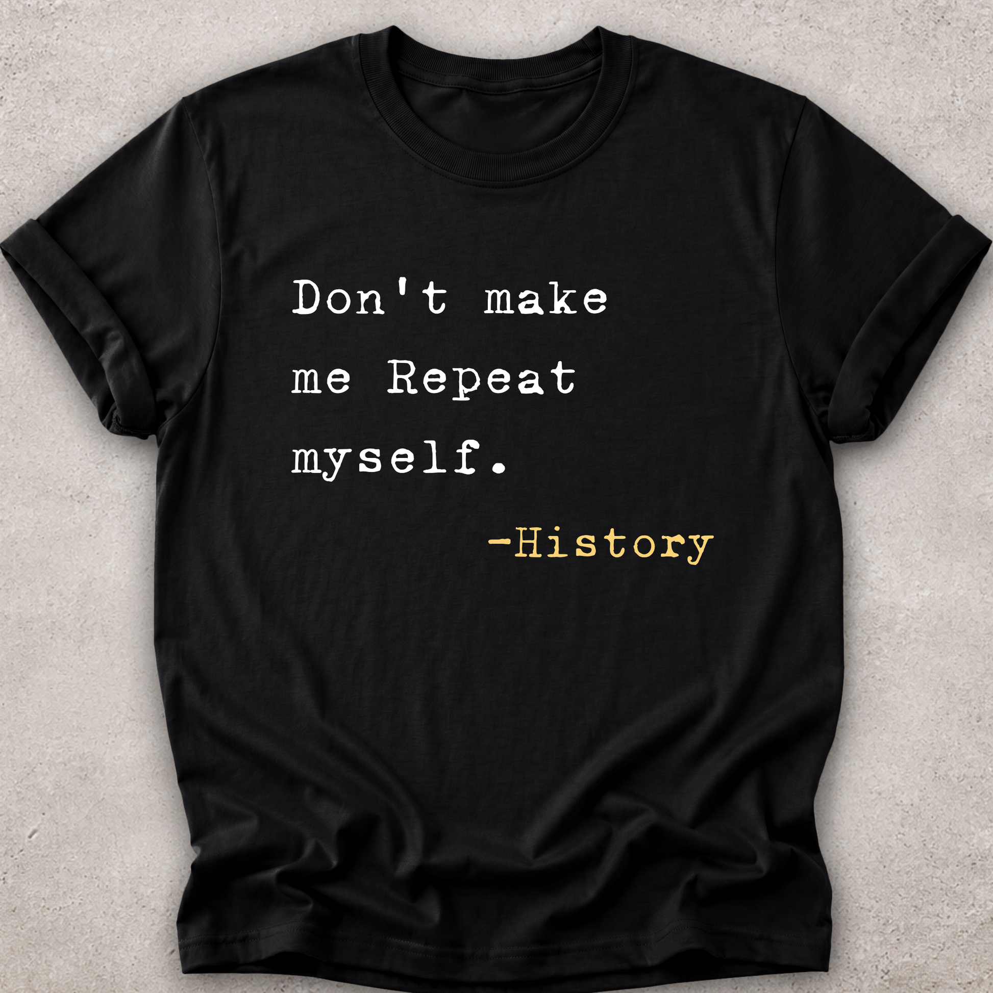 A black short-sleeve crewneck t-shirt laid flat on a textured light gray background. The shirt features a typewriter-style printed quote that reads 'Don't make me Repeat myself.
