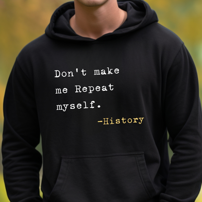 A person wearing a black hoodie with a printed quote on the chest that reads 'Don't make me Repeat myself. -History' in white and yellow text, photographed outdoors with a blurred green background.