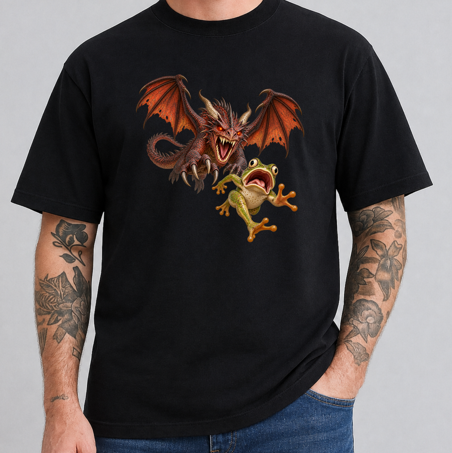 A man wearing a black short-sleeve t-shirt with a graphic print of a red dragon and a green frog, paired with blue jeans against a solid gray background.