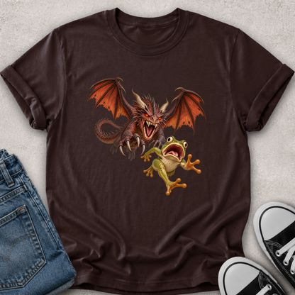 A dark brown short-sleeve t-shirt with a graphic of a red dragon and a green tree frog, styled in a flat lay with blue jeans and black-and-white sneakers on a light gray textured background.