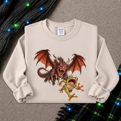 A cream-colored long-sleeve crewneck sweatshirt featuring a graphic print of a red dragon and a green frog, styled flat on a textured gray background with holiday lights and a plaid scarf.