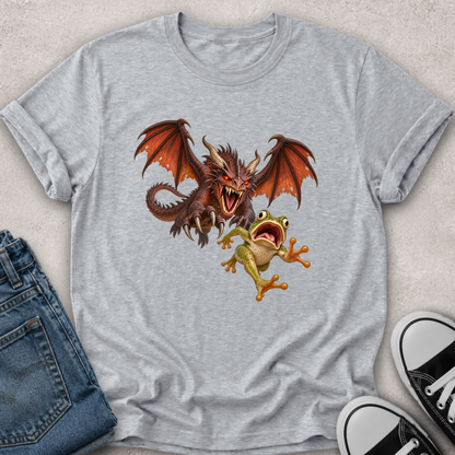 A light heather gray t-shirt featuring a graphic print of a red dragon and a green tree frog, styled in a flat-lay with blue jeans and black-and-white sneakers on a textured beige background.