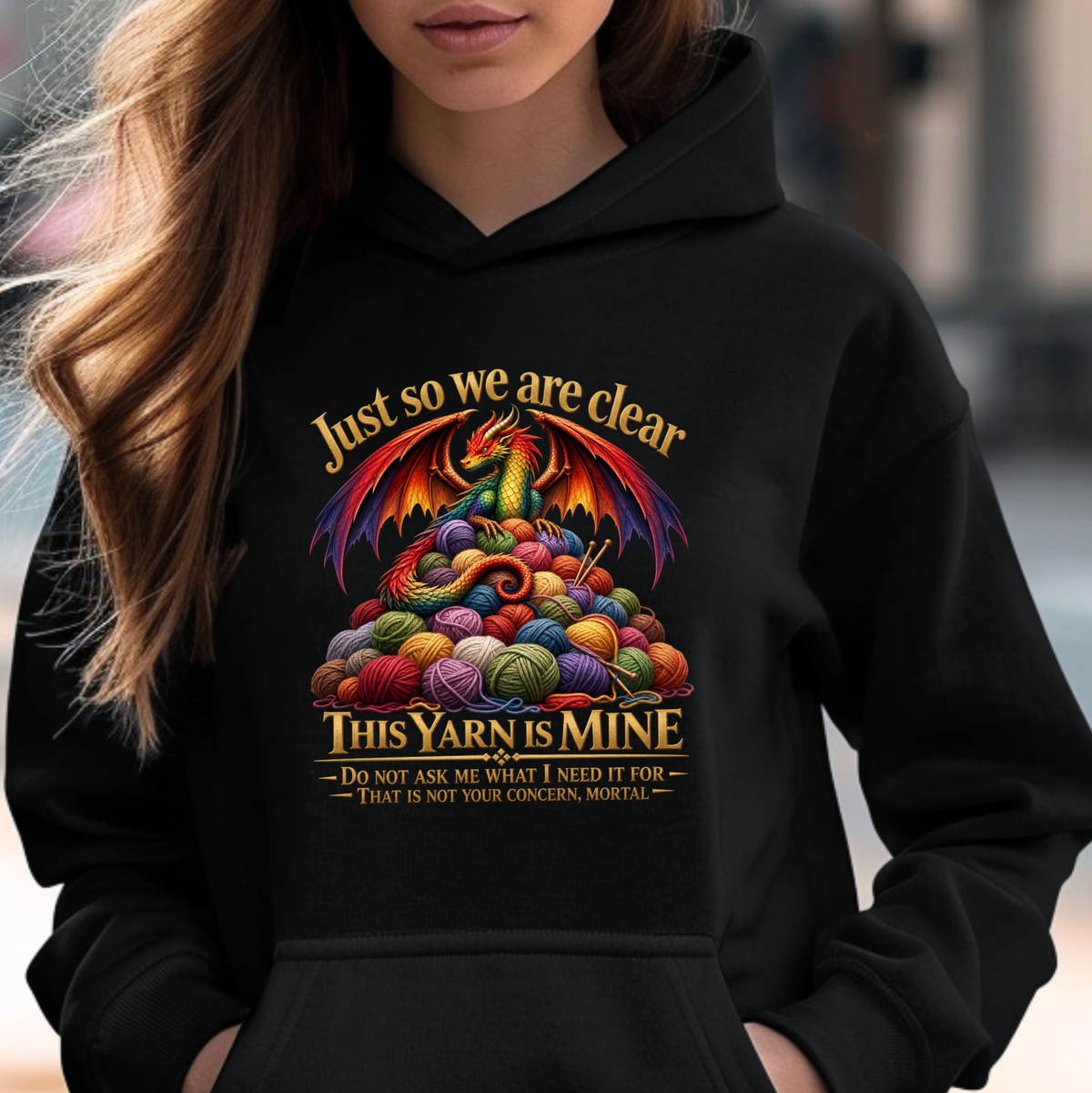A woman wearing a black hoodie with a colorful graphic of a dragon surrounded by balls of yarn and the text 'Just so we are clear THIS YARN IS MINE'.