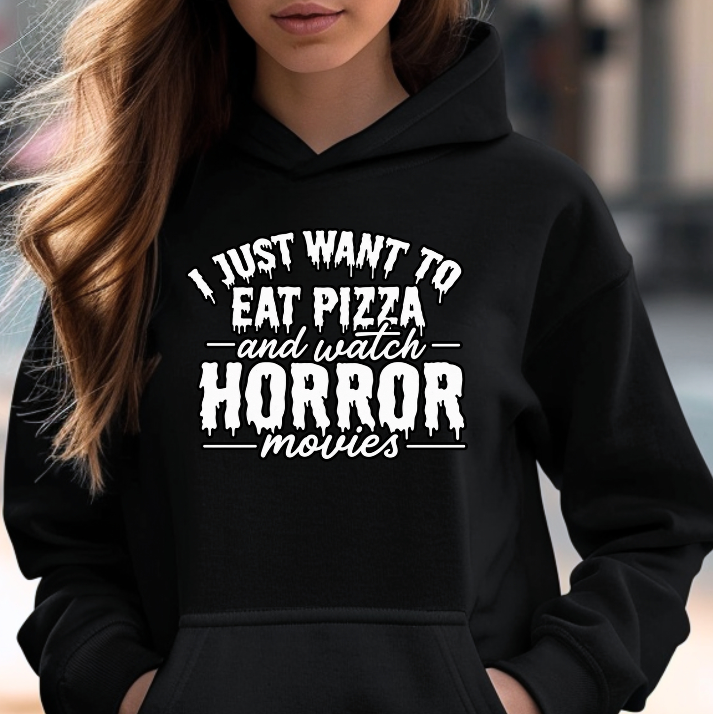 A woman wearing a black hoodie with a white graphic text print that reads 'I JUST WANT TO EAT PIZZA and watch HORROR movies'.