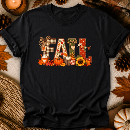 A black short-sleeve t-shirt with a colorful 'Fall' graphic print, styled in a flat-lay arrangement with autumn leaves, pinecones, and a lit candle.