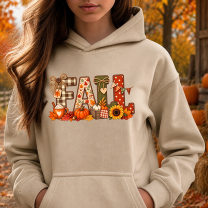A woman wearing a beige hoodie with a colorful 'Fall' graphic print featuring pumpkins, sunflowers, and autumn-themed patterns, set against an outdoor autumn background.